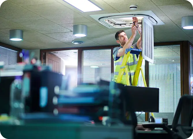 Man doing maintenance on a ventilation system inside an office